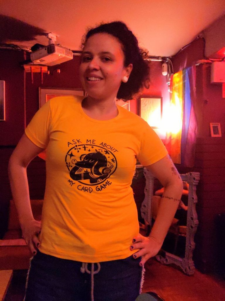 Talita wearing a t-shirt saying "ask me about my card game" with a dog drawing in it.